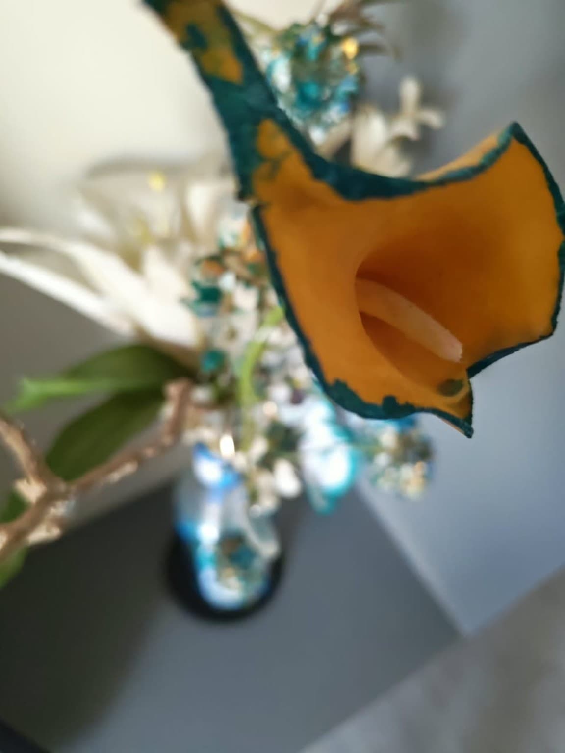 Orange calla lily with teal-painted edges emerging from a decorated bottle with white flowers and branches