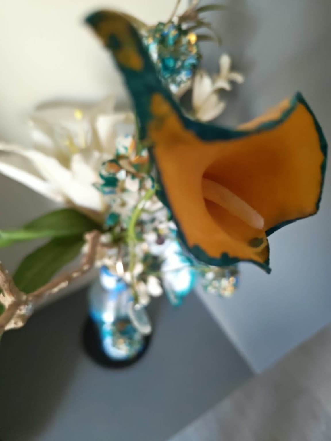 Close detail of an orange calla lily flower with deep teal painted edges against a soft grey background