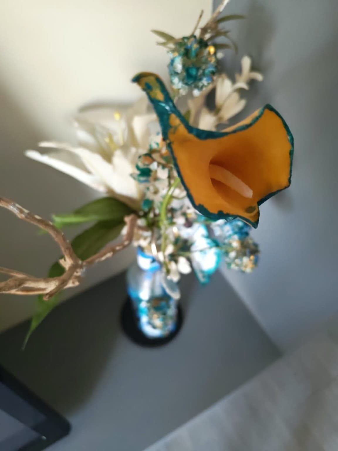 Full view of an upcycled bottle with teal and white painted botanical forms, orange calla lily and natural branches