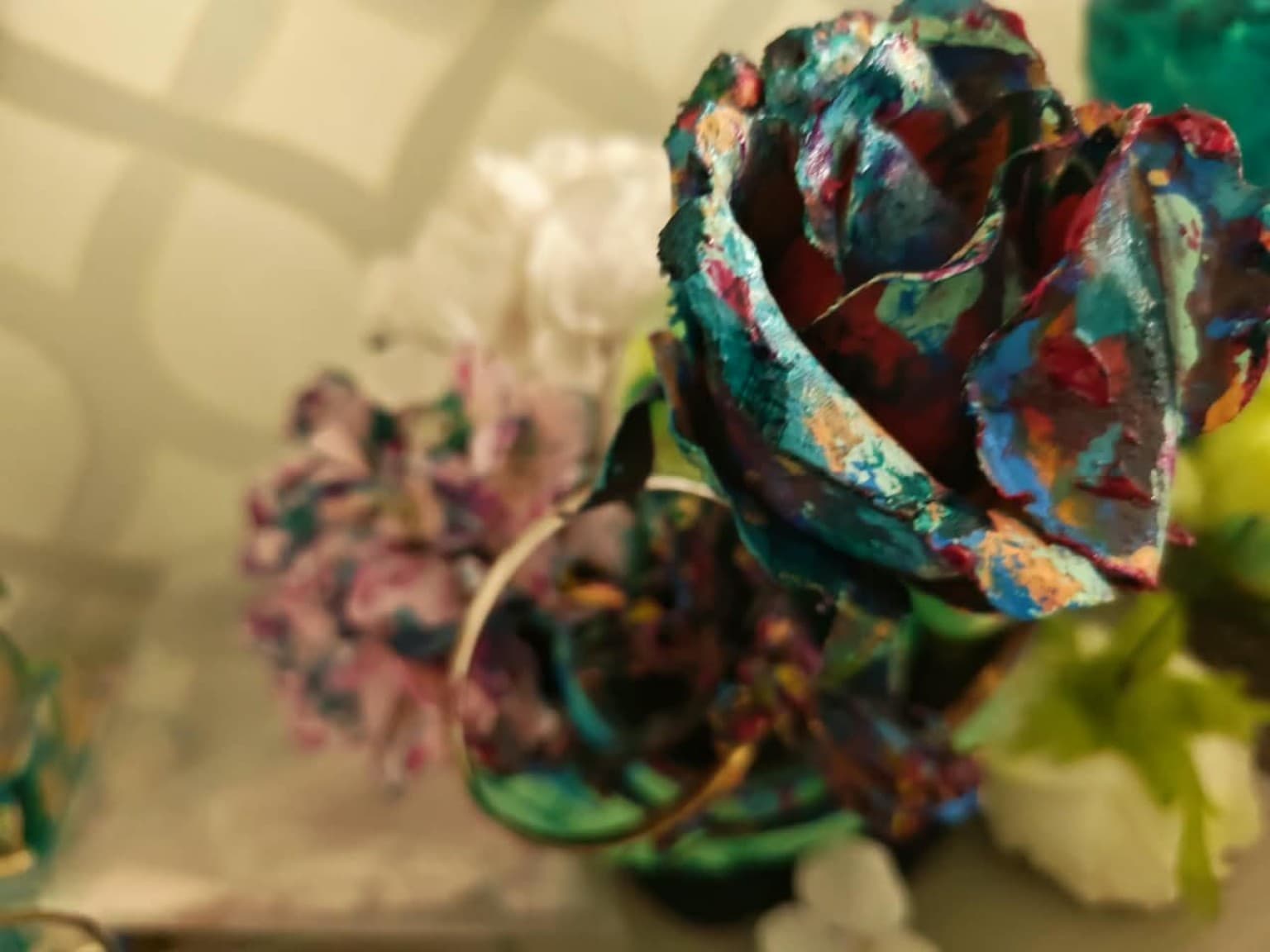 Close-up of a hand-painted sculptural rose with layered teal, crimson, blue and orange pigment on textured petals