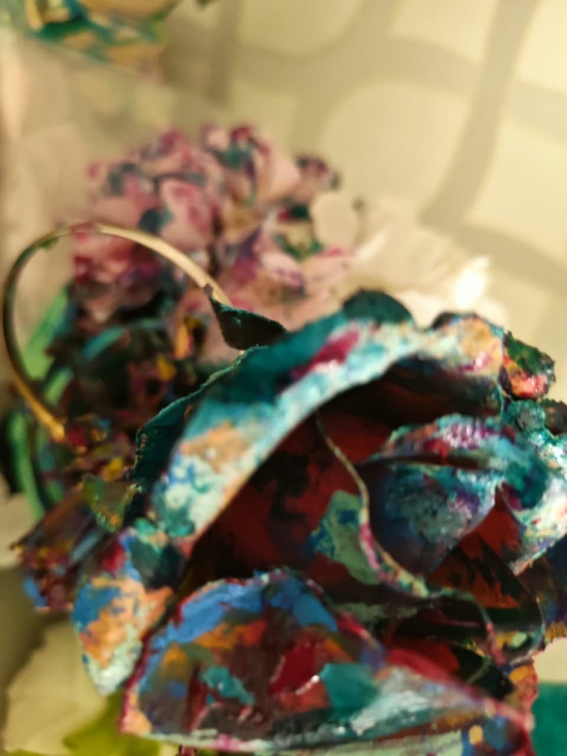 Macro view of a sculptural flower with visible brushstrokes in teal, crimson and blue over irregular handmade petals