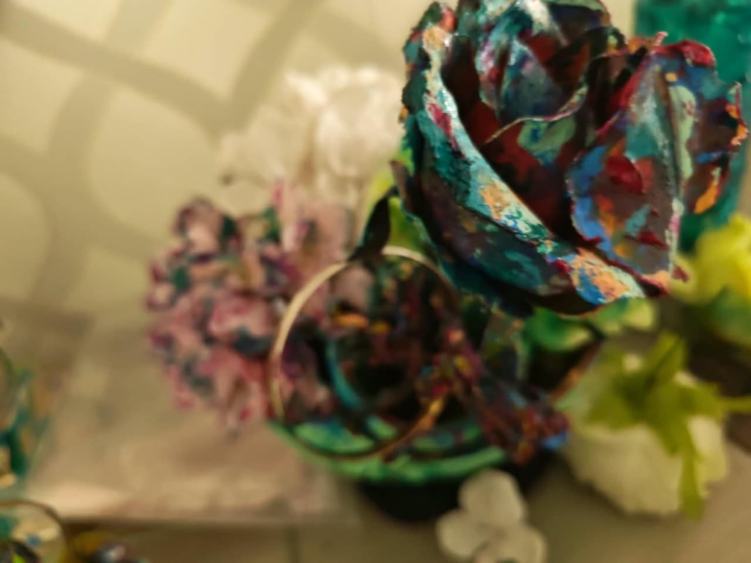 Wide view of hand-painted sculptural flowers with teal, crimson and blue pigment, with smaller flowers in the background