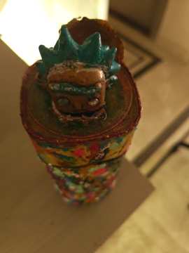 Small sculpted face with a turquoise crown-like form mounted on a colourful painted cylindrical object